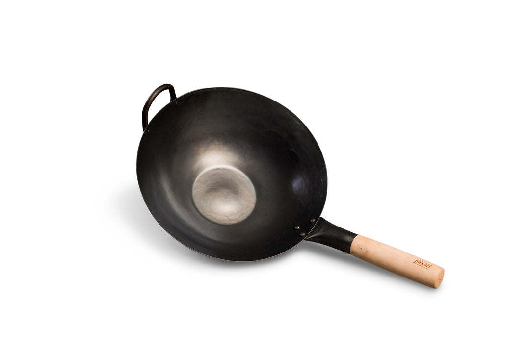 Vista oblicua del wok pasoli tradicionalmente martillado a mano y presazonado con fondo plano.
