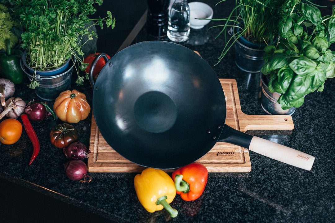 Traditionally hand-hammered pre-seasoned pasoli flat-bottomed wok carved on serving board and surrounded with appealing vegetables.