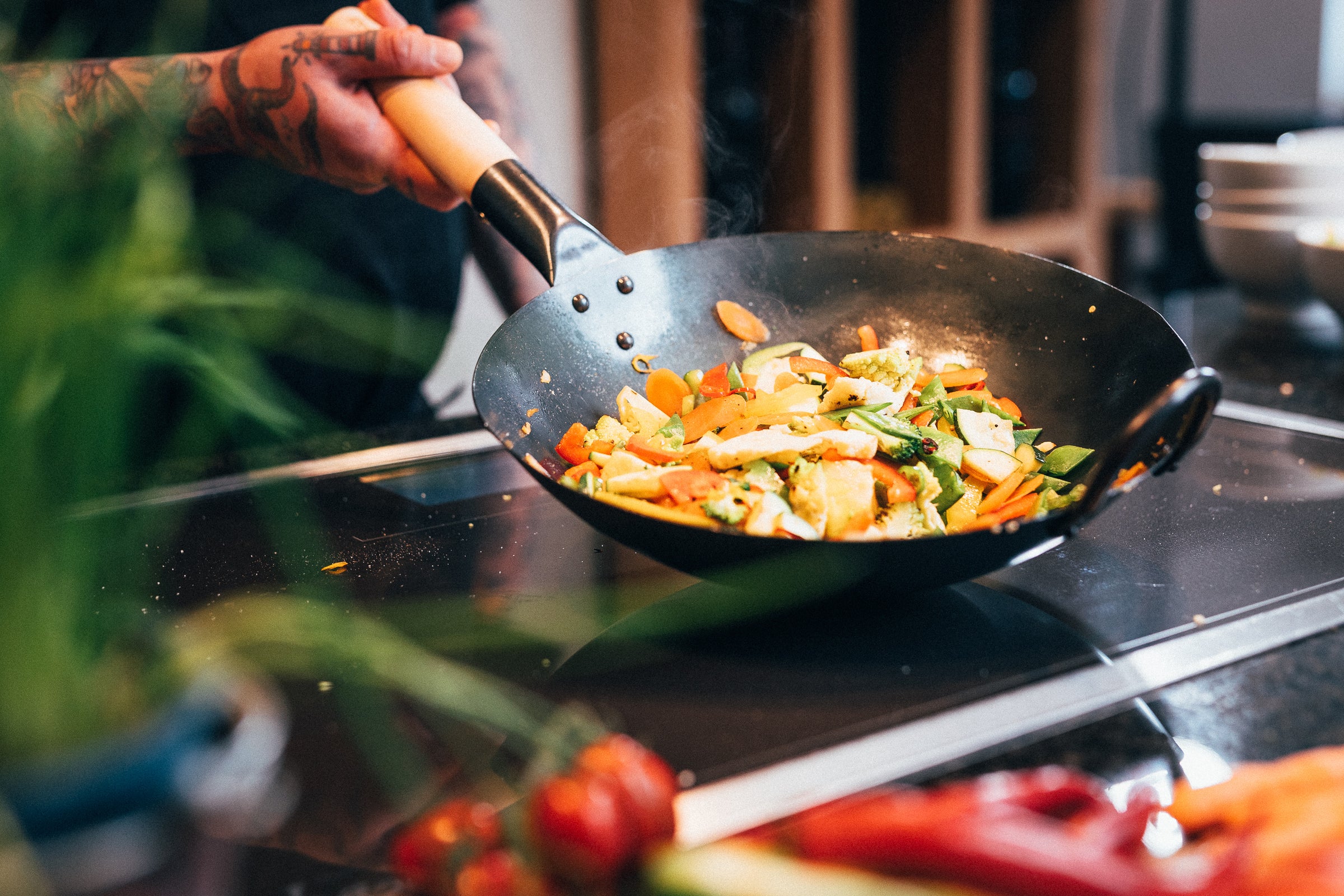 Traditionally hand-hammered pasoli wok with a flat base on induction in which a delicious vegetable pan is being cooked