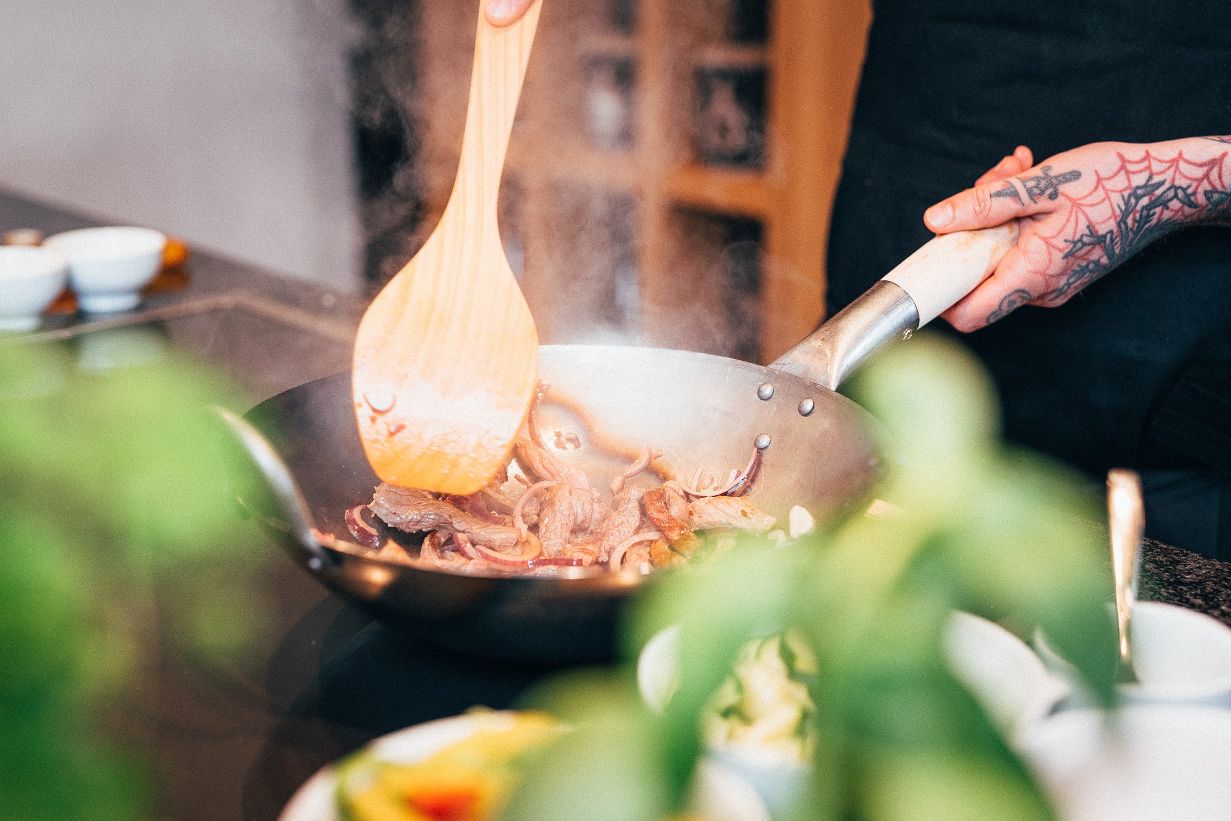 Nuestro chef profesional, Mane, saltea chuletas con cebolla en nuestro wok de fondo plano pasoli martillado a mano de forma tradicional, utilizando nuestra espátula de wok pasoli de madera de cerezo.